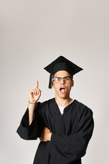Wall Mural - attractive young student in graduate outfit and vision glasses come up to idea on grey background