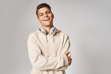 Wall Mural - handsome young guy in headphones smiling with folded arms against light background