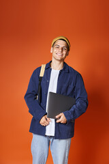 Wall Mural - charismatic guy in yellow hat with backpack holding laptop on terracotta background