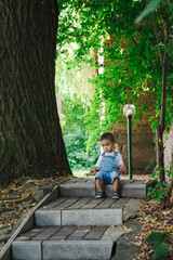 Sticker - Little boy sits on the steps in the park and looks at the camera.