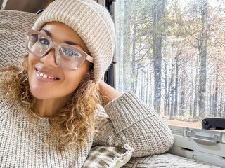 Wall Mural - Beautiful woman with woolen hat looks into the camera smiling. Lady sitting in the camper enjoying her holiday in the woods