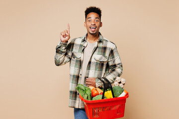 Wall Mural - Young man wears grey shirt hold red basket bag with food products point index finger up with great new idea isolated on plain pastel light beige background. Delivery service from shop or restaurant.