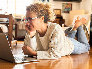 Wall Mural - One woman lay down on the floor at home using laptop computer smiling at screen. People and searching on web. Alternative small business workplace indoor leisure activity alone. Wireless connection