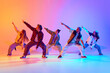 Group of five dancers in casual clothes performing with synchronized poses against gradient studio background in neon light. Concept of modern dance style, hobby, active lifestyle, youth culture