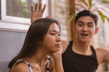 Wall Mural - Bored young woman unimpressed by her boyfriend's bragging and unverified tales on the couch in their living room. The couple appears to be in their early twenties.