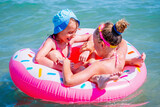 Fototapeta Natura - Portrait of two beautiful fun cool girls having fun in the sea on an inflatable circle. Summer holiday, rest, vacation, people, joy, happiness concept.