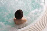 Fototapeta Uliczki - Boy sitting in the warm bubbling water jacuzzi. Happy kid relaxing in spa