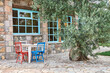 Stone house, decorative window, garden, wooden chair and table, olive-tree, outside.