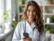 © garpinina - Sorridente, giovane e piacevole terapista medico di medicina generale in uniforme bianca che utilizza il telefono cellulare per videochiamare un paziente