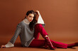 Fashionable confident woman wearing stylish striped woolen sweater, red jeans, patent leather  ankle boots, posing on brown background. Studio fashion portrait. Copy, empty, blank space for text
