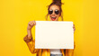 Mulher feliz com roupas fashion segurando um cartaz em branco isolada no fundo amarelo