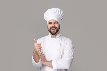 Canvas Print - Happy young chef in uniform showing thumb up on grey background