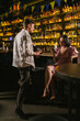 © SlavaStock - Colleagues tired after party near cozy bar counter. Lady sits with cellphone near standing upset friend at meeting in night club