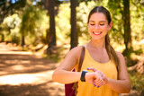 Fototapeta  - Young Active Woman Checking Activity Monitor On Smart Watch Hiking Along Trail Through Countryside