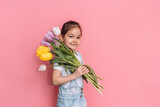 Fototapeta Maki - A child carries a bouquet of tulips on his shoulder against a pink background.