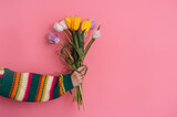 Fototapeta Maki - Side view of woman's hand holding a bouquet of tulips against a pink background.