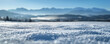 A panoramic view of a high alpine meadow under a blanket of snow, the detail of the snow surface crisp against a blurred backdrop of distant mountains \