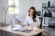 © Wasana - A young woman concentrated on budgeting with papers and laptop in a home office.