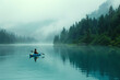 Person kayaking on a serene misty lake with forested mountains. Peaceful nature adventure photography. Solitude and tranquility concept. Design for poster, banner, and wellness retreats.