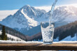 Pouring water from bottle into a glass on a background of winter landscape of mountains.  natural water. generative ai