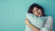 Closeup sleepy beautiful woman with closed eyes hugging soft pillow on isolated light pastel blue background with space for copy