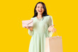 Beautiful young woman with shopping bag and purse on orange background