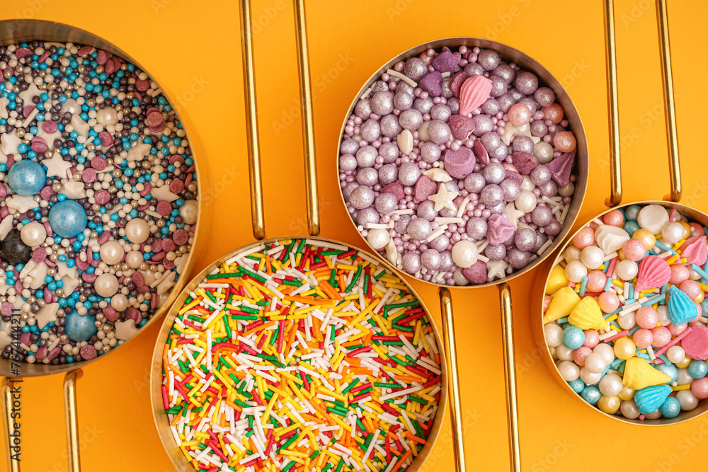 Measuring cups with sweet colorful sprinkles on orange background