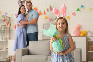 Wall Mural - Happy parents and their daughter in bunny ears with Easter gift at home