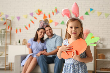 Wall Mural - Happy parents and their daughter in Easter bunny ears holding paper carrot at home