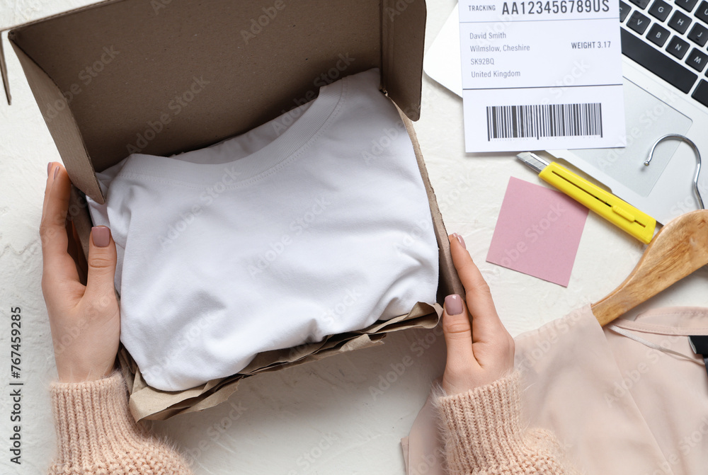 Woman opening parcel with clothes at white table