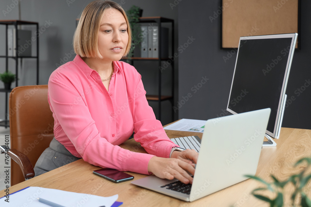 Mature businesswoman working with laptop and computer in modern office