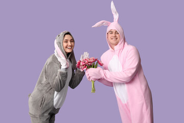 Wall Mural - Beautiful young couple in bunny costume with bouquet of tulips on purple background. Easter celebration