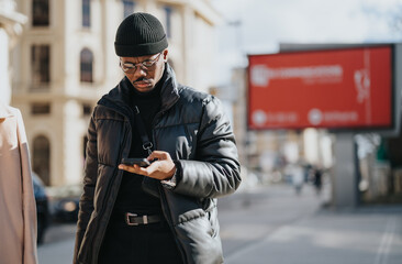 Wall Mural - Young businessman using smart phone on urban street with billboards.