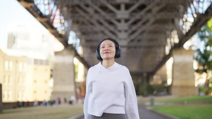 Wall Mural - 4K Asian woman in sportswear listening to music with headphones and mobile phone app jogging workout exercise at city street in the morning. Healthy care motivation sport training and running concept.