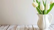  a white vase filled with white tulips on top of a wooden table in front of a white wall.
