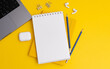 Top view composition with yellow notebook and pens placed near laptop and headphones on yellow background