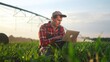 © maxximmm - corn agriculture. a male farmer works on a laptop in a field with green corn sprouts. lifestyle corn is watered by irrigation machine. irrigation agriculture business concept