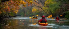 A Group Of Friends On A Kayaking Adventure Enjoy The Serene Waters Of A River Surrounded By The Colorful Foliage Of Autumn.