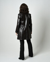 Poster - Full length portrait of brunette woman wearing long leather trench coat and black boots. Standing pose walking away from camera, facing backwards. Isolated silhouette on white studio background.