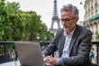 © PixelGallery - Mature businessman using laptop in Paris, France. Eiffel tower in the background