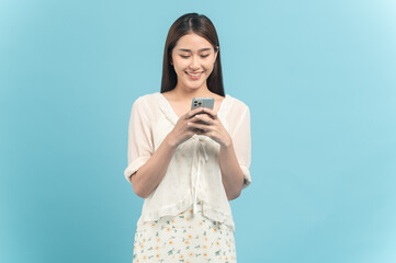 Wall Mural - Beautiful young asian woman in white dress with flower pattern using smartphone isolated on blue background