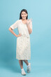 Beautiful young asian woman in white dress with flower pattern making okay sign isolated on blue background