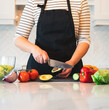 © Cavan Images - Torso of woman in apron chopping vegetables in white kitchen.
