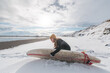 © Cavan Images - Woman standing on beach with surf board winter iceland