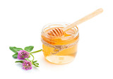 Fototapeta Sypialnia - Glass jar of sweet fresh honey, wooden honey dipper and clover flower on a white background. Selective focus, front view, close-up.