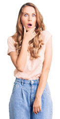 Poster - Young beautiful caucasian woman with blond hair wearing casual clothes looking fascinated with disbelief, surprise and amazed expression with hands on chin