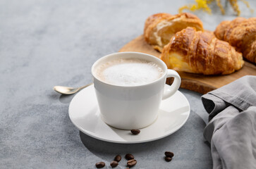 Wall Mural - A cup of aromatic cappuccino coffee and fresh croissants on a blue background with coffee beans and flowers. The concept of a delicious and healthy breakfast with homemade cakes. Copy space.