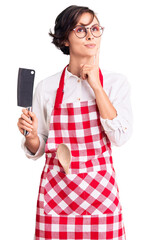 Poster - Beautiful young woman with short hair wearing professional baker apron holding knife serious face thinking about question with hand on chin, thoughtful about confusing idea