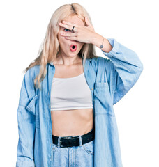 Wall Mural - Young caucasian woman wearing casual clothes peeking in shock covering face and eyes with hand, looking through fingers afraid