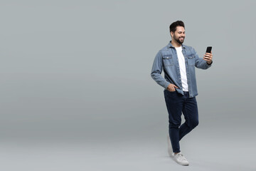 Poster - Happy young man using smartphone on grey background, space for text